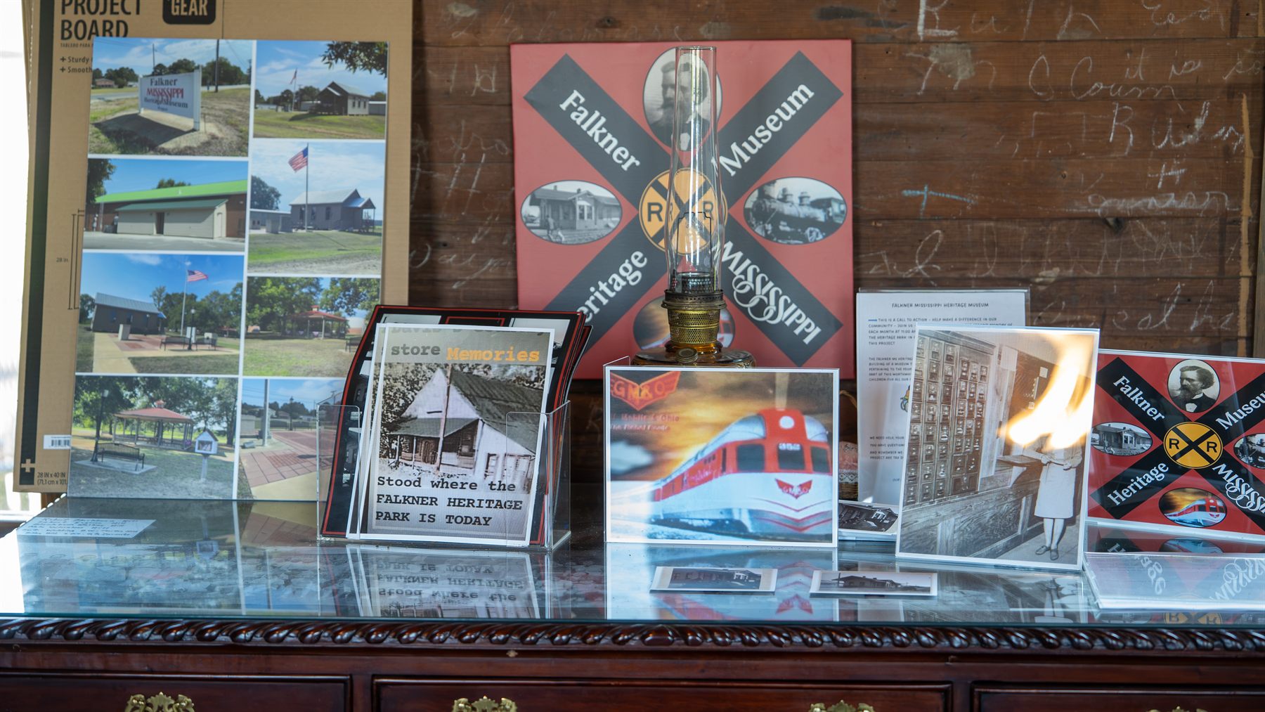 Museum display inside the Cooper Hill School House: the Falkner Mississippi Heritage crossbuck sign, an oil lamp, historic depot photographs and railroad memorabilia arranged on a wooden sideboard.