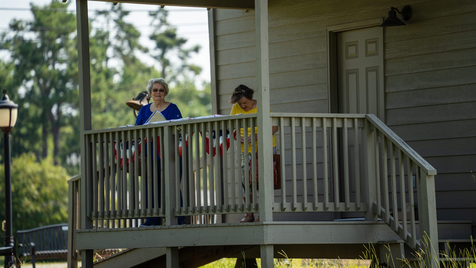 Two Falkner Heritage volunteers hanging patriotic bunting along the porch rail of the Cooper Hill School House.